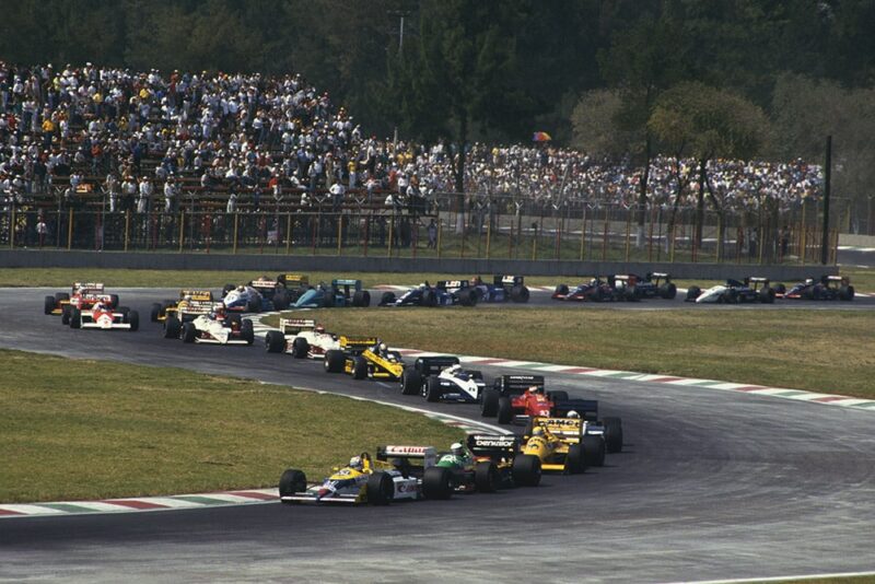 Nigel Mansell (Williams FW11B Honda) 1st position, leads Teo Fabi (Benetton B187 Ford), Ayrton Senna (Lotus 99T Honda) and the rest of the field on the first lap of the Mexican GP.