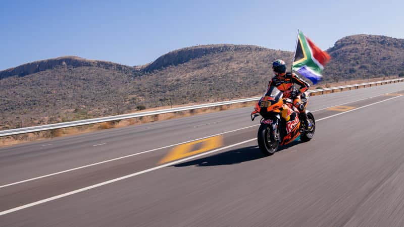 Brad Binder rides KTM RC16 while holding a South African flag