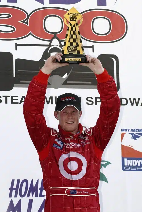 oyota racing driver holds a trophy above his head.