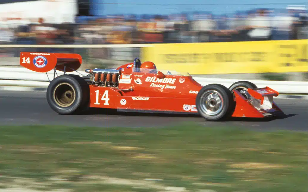 Vintage red No.14 Gilmore Racing Team IndyCar with exposed engine and rear wing driven at speed