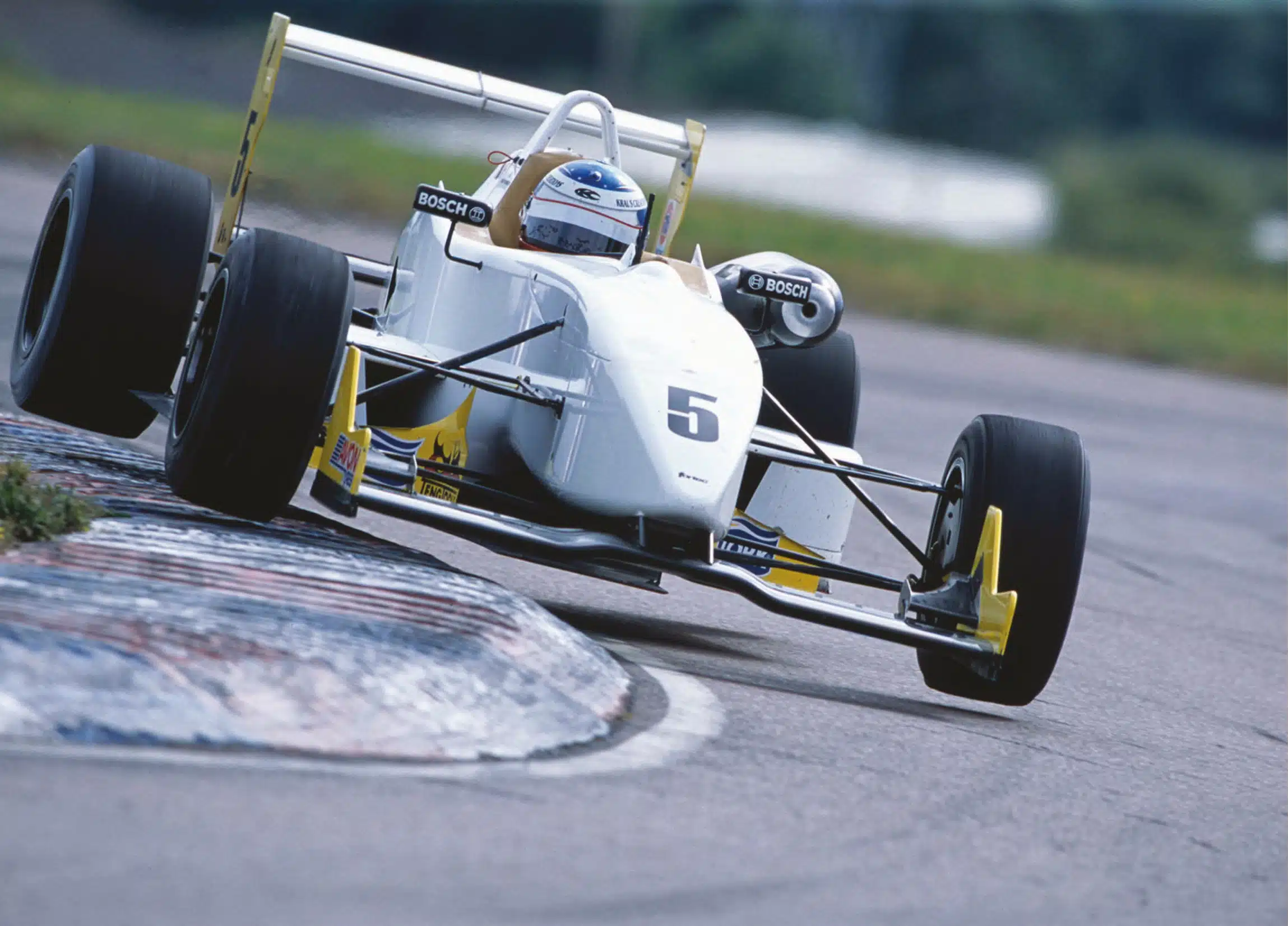 White No.5 Bosch Formula race car cornering with front wheel lifted over red white blue curb