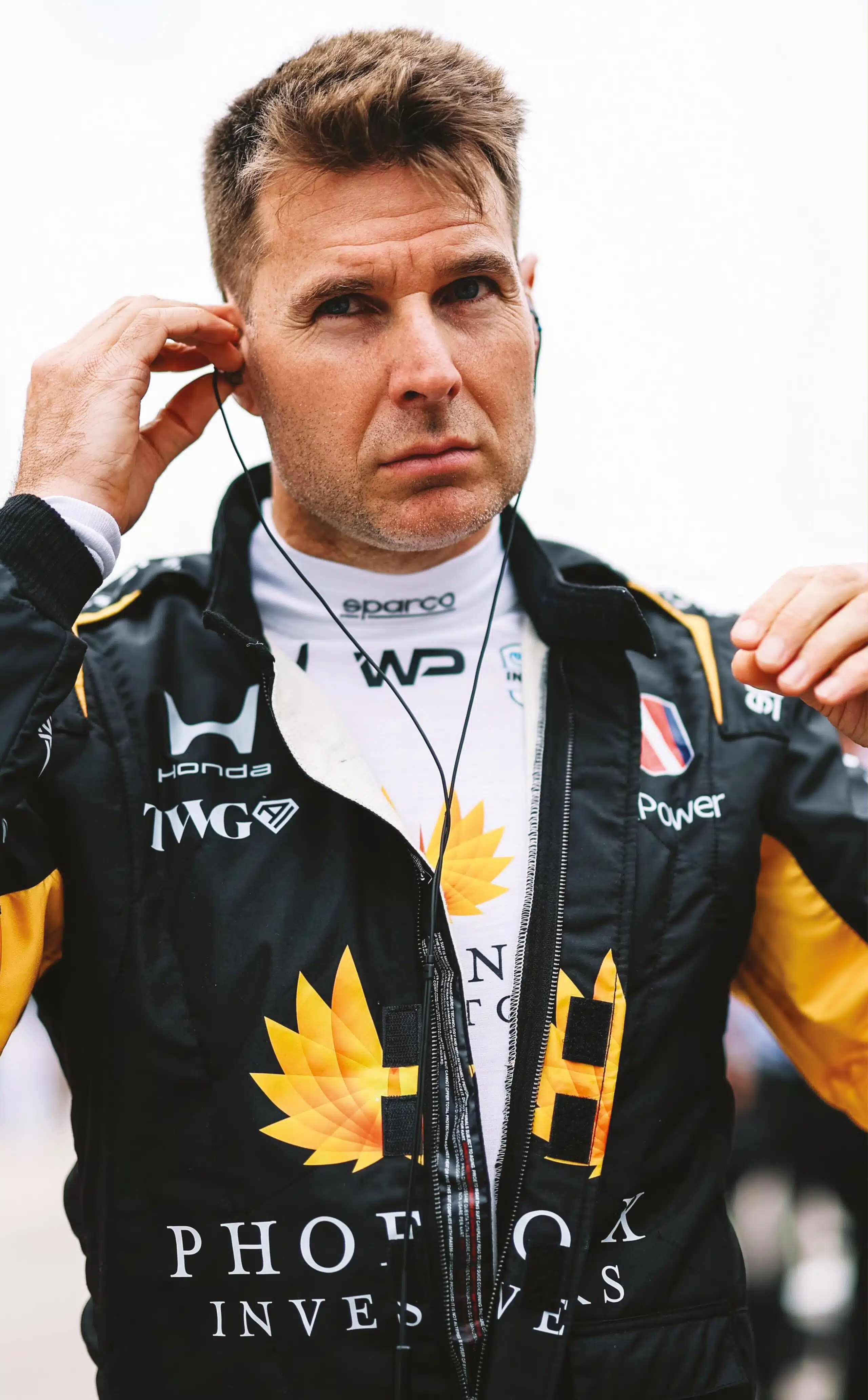 Will Power in black yellow TWG Honda Sparco racing suit adjusts earphones before IndyCar race